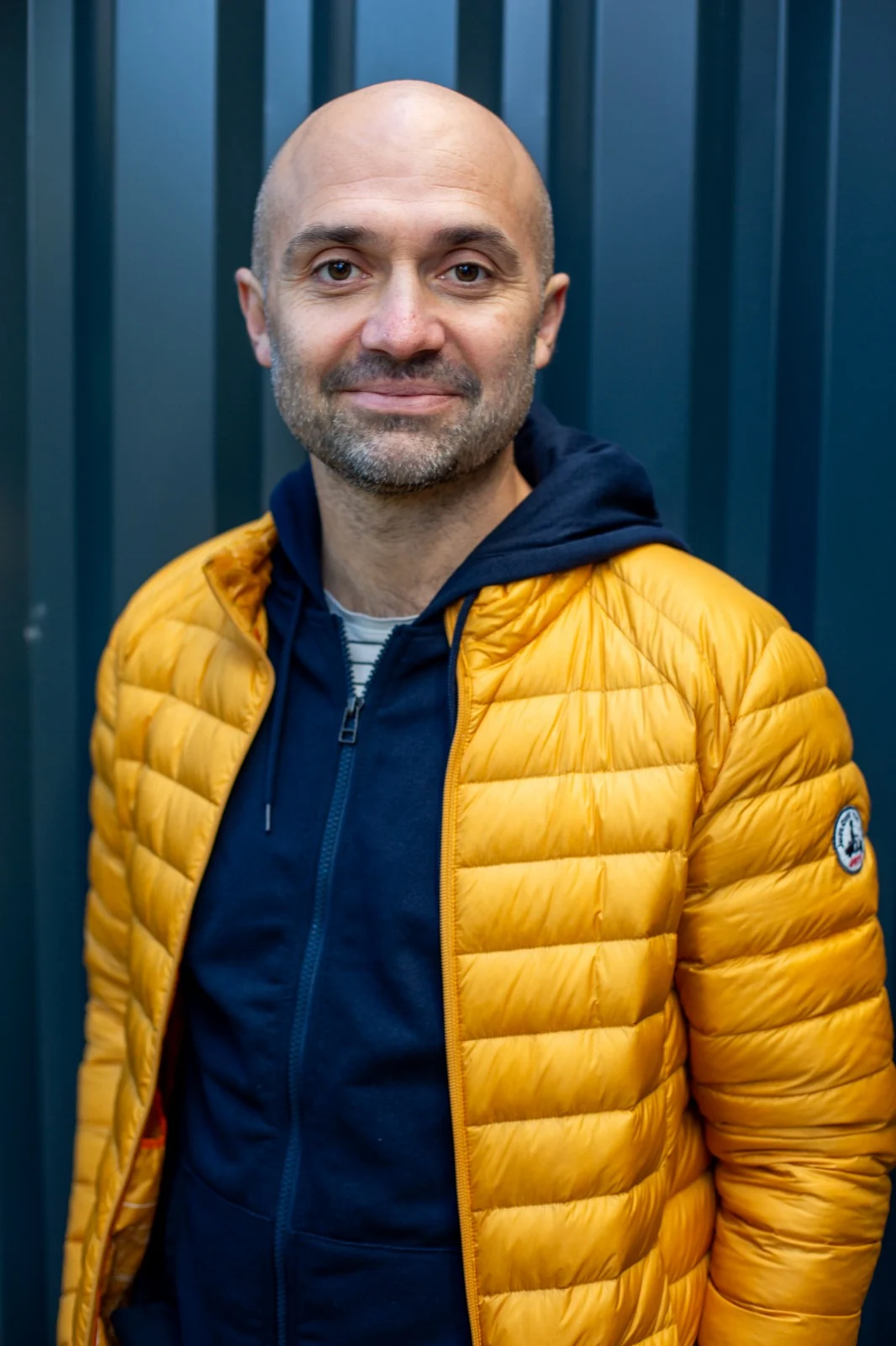 Christophe Jacques, veste jaune, sourit devant un mur bleu nuit