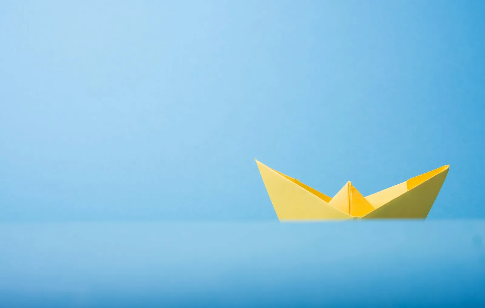 Un bateau en papier jaune flotte sur une eau bleue et calme