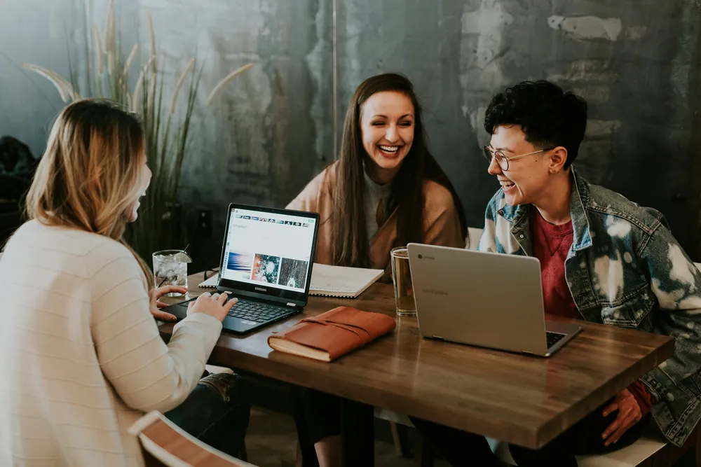 Trois collègues rient ensemble autour d’une table de travail