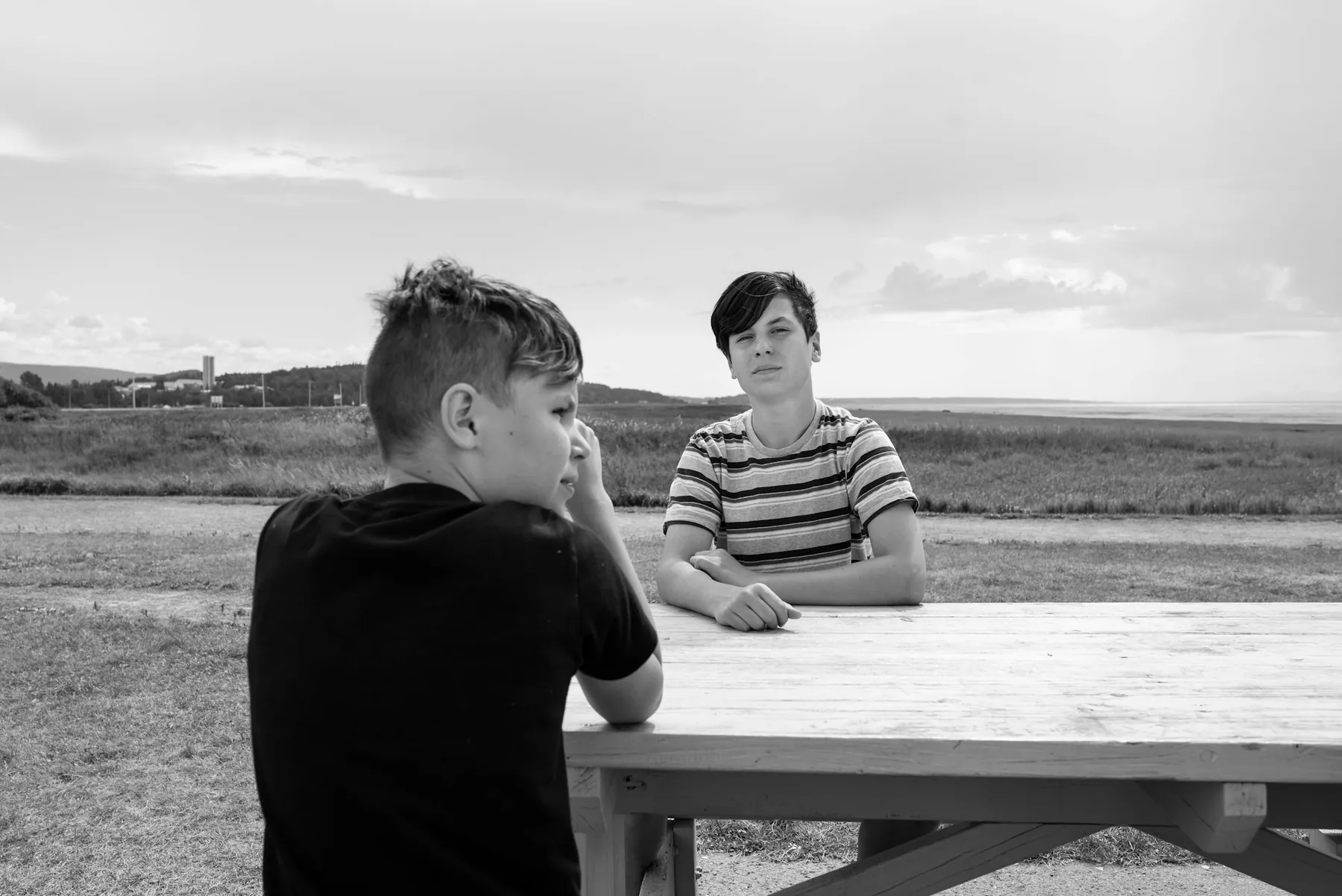 Deux adolescents discutent, assis à une table en plein air